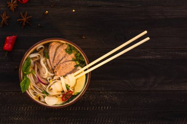 Vietnam baharatlı pho bo çorbası, pirinç eriştesi, sığır eti dilimleri, kırmızı biber, kişniş, soğan, kahverengi ahşap arka planda yıldız anason..