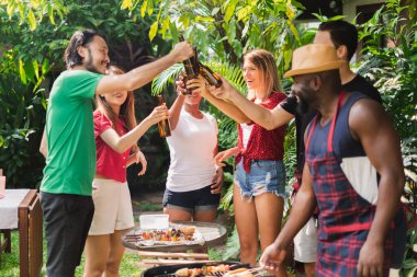 Bir grup farklı insan evde barbekü / barbekü partisi veriyor, öğle yemeğinde ızgara et / biftek pişiriyor, mutlu arkadaşlar parti yaşam tarzı kavramı