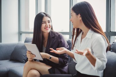Takım elbiseli iki Asyalı iş kadını internet alışverişi, internet bankacılığı ve internet üzerinden hizmet satın almak için akıllı telefon kullanıyor..
