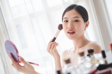Genç, güzel bir Asyalı kadın yüzüne makyaj malzemesi sürüyor. Güzellik bakımı ve makyaj konsepti.