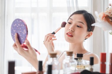 Genç, güzel bir Asyalı kadın yüzüne makyaj malzemesi sürüyor. Güzellik bakımı ve makyaj konsepti.