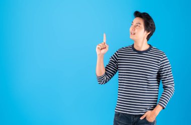 Genç yakışıklı Asyalı adam / mutlu adam yukarıdaki fotokopi alanını işaret ediyor. Mavi arka plan üzerinde izole edilmiş, stüdyo çekimi.