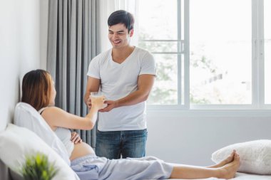 Genç Asyalı koca hamile karısına bir bardak kalsiyum sütü veriyor.