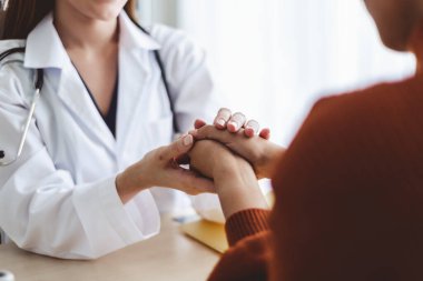 Asyalı doktor kadın, genç kadını el ele tutuşarak cesaretlendiriyor.
