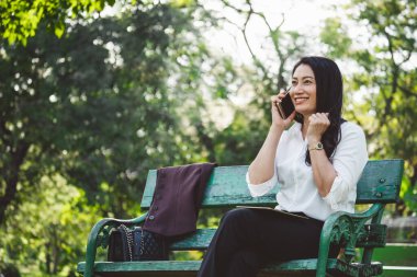 Asyalı iş kadını parkın dışındaki cep telefonuyla konuşurken iyi haberler veriyor.