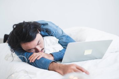 Çok çalıştıktan sonra beyaz yatakta uyuyan yorgun Asyalı genç adam.