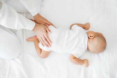 Genç Asyalı anne yeni doğmuş bebeğine beyaz yatakta sevgiyle dokunuyor. Anneler günü konsepti.