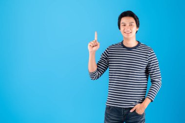 Genç yakışıklı Asyalı adam / mutlu adam yukarıdaki fotokopi alanını işaret ediyor. Mavi arka plan üzerinde izole edilmiş, stüdyo çekimi.