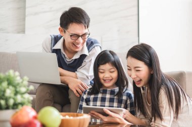 Tablet kullanan mutlu Asyalı aile, oyun oynamak için dizüstü bilgisayar film izlemek, yaşam tarzı konsepti için evde dinlenmek.
