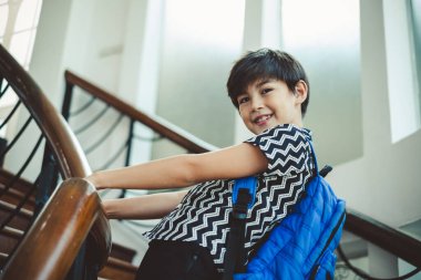 Okul çantasıyla yerde duran sevimli çocuk, fotokopi çekerek gülümsüyor.