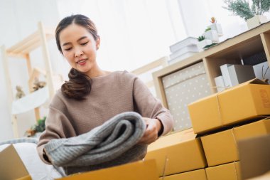 Genç Asyalı kadın satıcı çevrimiçi iş, çevrimiçi alışveriş, nakliye kutusu ve paket için kıyafet paketi yapıyor.