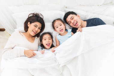 Mutlu Asyalı aile yatak odasında uzanıyor, gülümsüyor ve gülümsüyor.