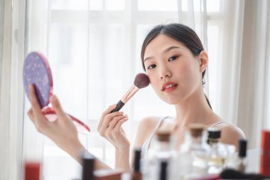 Genç, güzel bir Asyalı kadın yüzüne makyaj malzemesi sürüyor. Güzellik bakımı ve makyaj konsepti.