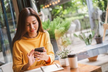 Genç Asyalı güzel bir kadın akıllı telefonu iş için kullanıyor, online alışveriş, para transferi, finans, internet bankacılığı. Kafede arka planda bulanıklık var..