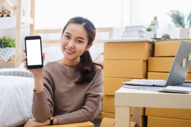 Genç Asyalı kadın satıcı internet işi, çevrimiçi alışveriş, nakliye, kutu ve paket konsepti için yeri olan bir telefon ekranı gösteriyor.