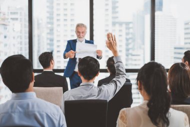 Bir grup iş adamı toplantı odasındaki seminerde soru sormak ve konuşmacılara cevap vermek için ellerini kaldırıyor.