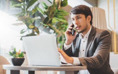 Ofiste çalışırken bilgisayar ve cep telefonu kullanan Asyalı işadamı