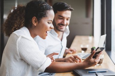Genç adam ve kadın dizüstü bilgisayarda çalışıyor ve cep telefonu kullanıyor. İş yerinde rahatlayın.