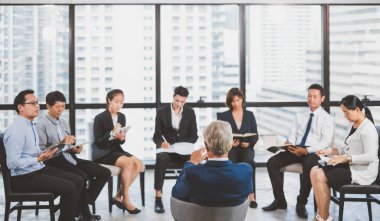 Bir grup iş adamı toplantı odasındaki seminerde soru sormak ve konuşmacılara cevap vermek için ellerini kaldırıyor.