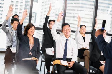 Bir grup iş adamı toplantı odasındaki seminerde soru sormak ve konuşmacılara cevap vermek için ellerini kaldırıyor.
