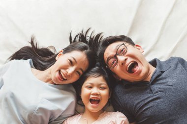 Mutlu Asyalı aile yatak odasında uzanıyor, gülümsüyor ve gülümsüyor.