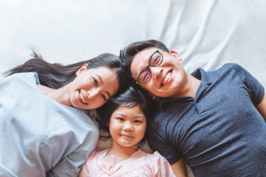 Mutlu Asyalı aile yatak odasında uzanıyor, gülümsüyor ve gülümsüyor.
