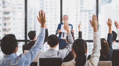 Bir grup iş adamı toplantı odasındaki seminerde soru sormak ve konuşmacılara cevap vermek için ellerini kaldırıyor.