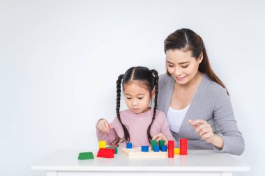 Asyalı kız çocuğu, beyaz arka planda annesiyle blok oyuncağı oynuyor. Mutlu aile kavramı.