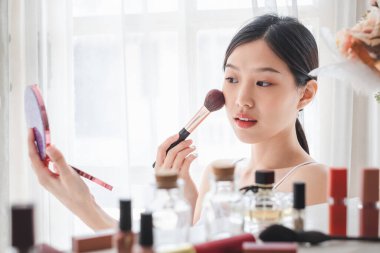 Genç, güzel bir Asyalı kadın yüzüne makyaj malzemesi sürüyor. Güzellik bakımı ve makyaj konsepti.