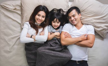 Mutlu Asyalı aile yatak odasında uzanıyor, gülümsüyor ve gülümsüyor.