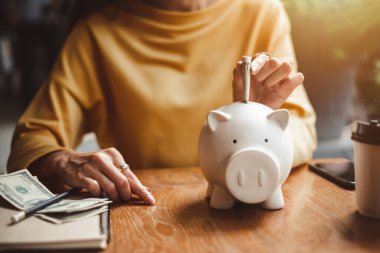 Kadın, para biriktirmek ve finansal konsept için domuzcuğa banknot dolar koyuyor..