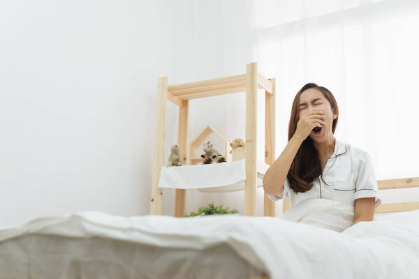 Азиатка просыпается утром, сидя на белой кровати и растягиваясь, чувствуя себя счастливой и свежей