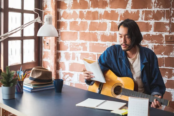 Asian man musician writing song with guitar