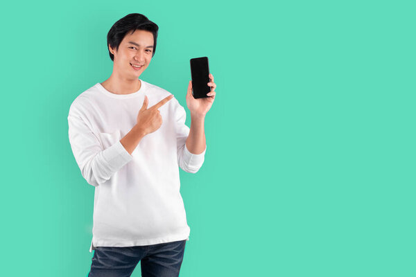 Young Asian man pointing to mobile phone with happy and cheerful over green background with copy space