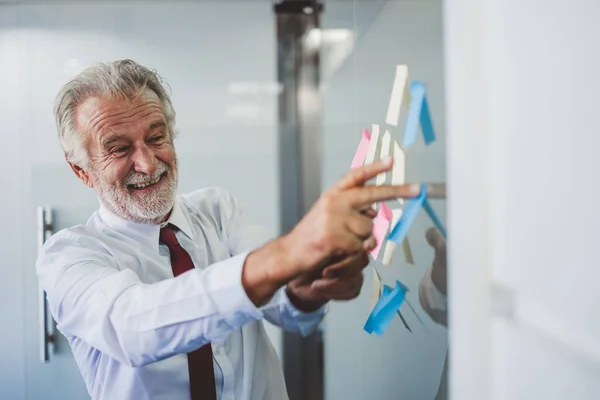 Old senior business man happy working in office, reading sticky note post it in room