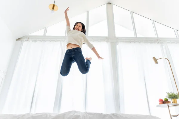 若いですアジアの女性ジャンプオンホワイトベッドでベッドルーム 幸せな生活とライフスタイルに家 — ストック写真