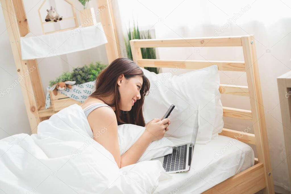 Beautiful Asian woman using laptop and smart phone in bed room for online shopping, Asian woman lifestyle concept