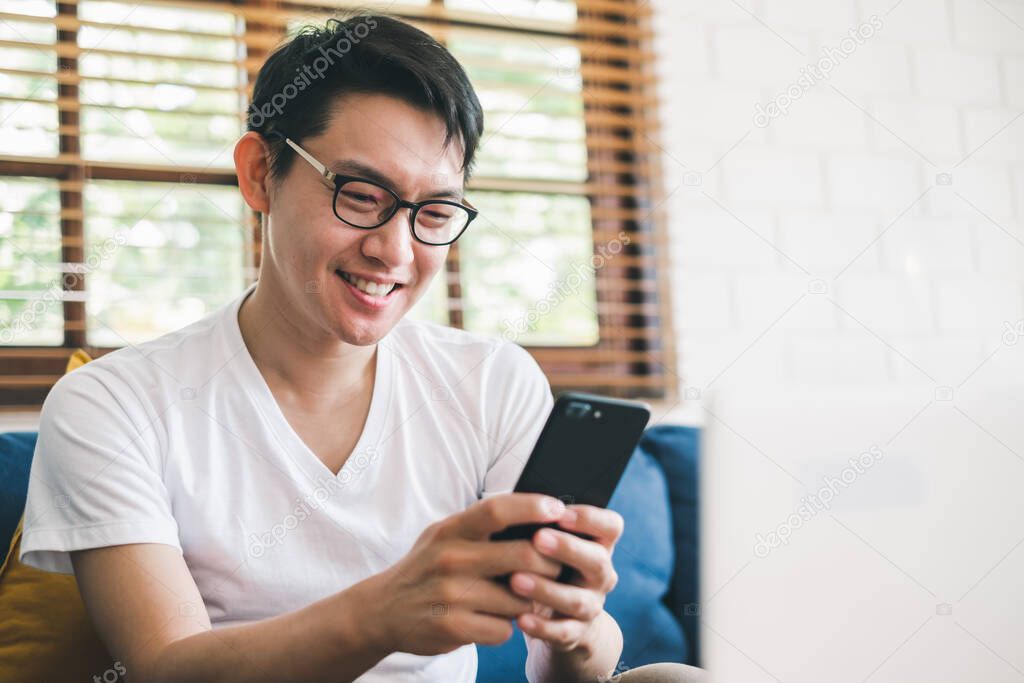 Young Asian man using phone for online shopping, and working with laptop at home