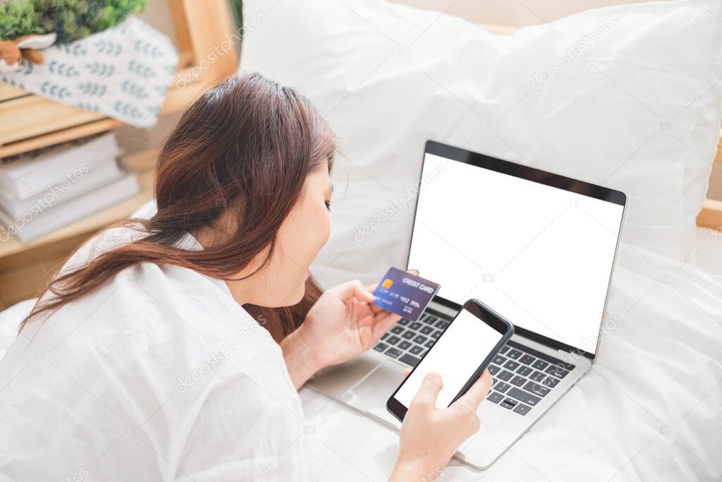 Beautiful Asian woman using laptop and smart phone in bed room for online shopping, Asian woman lifestyle concept