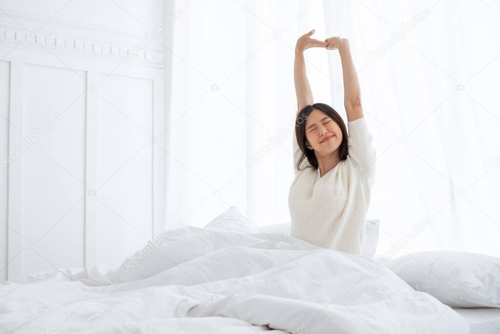 Asian woman wake up in the morning, sitting on white bed and stretching, feeling happy and fresh