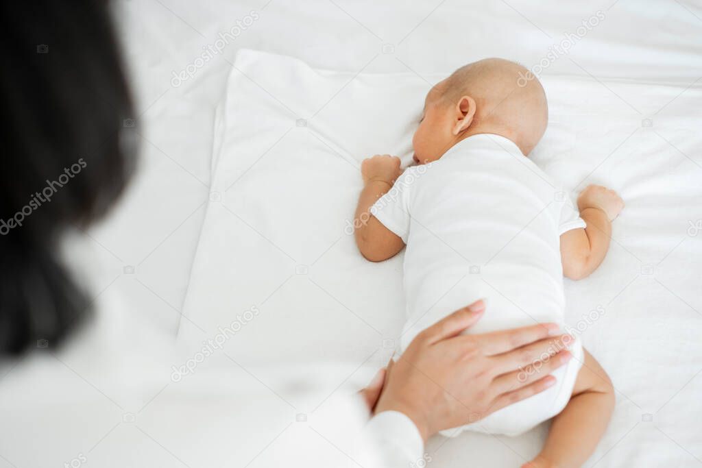 Young Asian mother touching her newborn baby with love on white bed, mother's day concept