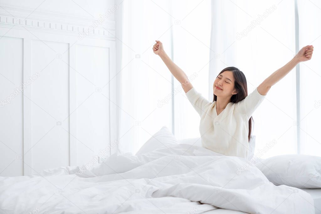 Asian woman wake up in the morning, sitting on white bed and stretching, feeling happy and fresh