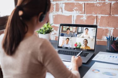 Genç Asyalı iş kadını iş arkadaşlarıyla evde çalışıyor ve iş arkadaşlarıyla sanal video konferansı yapıyor, internet üzerinden çalışıyor, evdeki sosyal mesafeler nedeniyle video görüşmesi yapıyor.