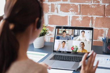 Genç Asyalı iş kadını iş arkadaşlarıyla evde çalışıyor ve iş arkadaşlarıyla sanal video konferansı yapıyor, internet üzerinden çalışıyor, evdeki sosyal mesafeler nedeniyle video görüşmesi yapıyor.