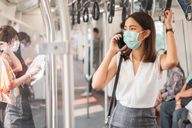 Coronavirus (Covid-19) konsepti, Coronavirus covid-19 'dan korunmak için koruyucu yüz maskesi takan Asyalı kadın gökyüzü treninde dikiliyor ve insanlar kalabalıklaşıyor.