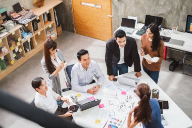 Bir grup Asyalı iş adamı ve yaratıcı tasarımcı ofisinde toplanıyor.