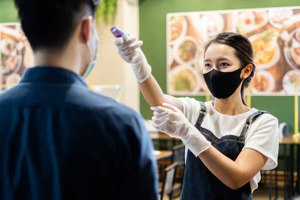 Asyalı restoran garsonu gripten ve Coronavirus covid-19 'dan korunmak için restorana girmeden önce termometreyle koruyucu yüz maskesi takıyor.