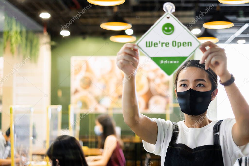 Business owner Asian woman wear protective face mask ppe hanging open sign at her restaurant / cafe open again after lock down due to outbreak of coronavirus covid-19