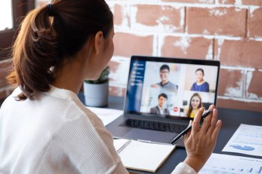 Genç Asyalı iş kadını iş arkadaşlarıyla evde çalışıyor ve iş arkadaşlarıyla sanal video konferansı yapıyor, internet üzerinden çalışıyor, evdeki sosyal mesafeler nedeniyle video görüşmesi yapıyor.