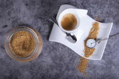 Beyaz porselen kahve bardağı kahverengi şeker, şeker kase ve cep saati ile köpük sıcak bir kahve için zaman olduğunu gösterir.